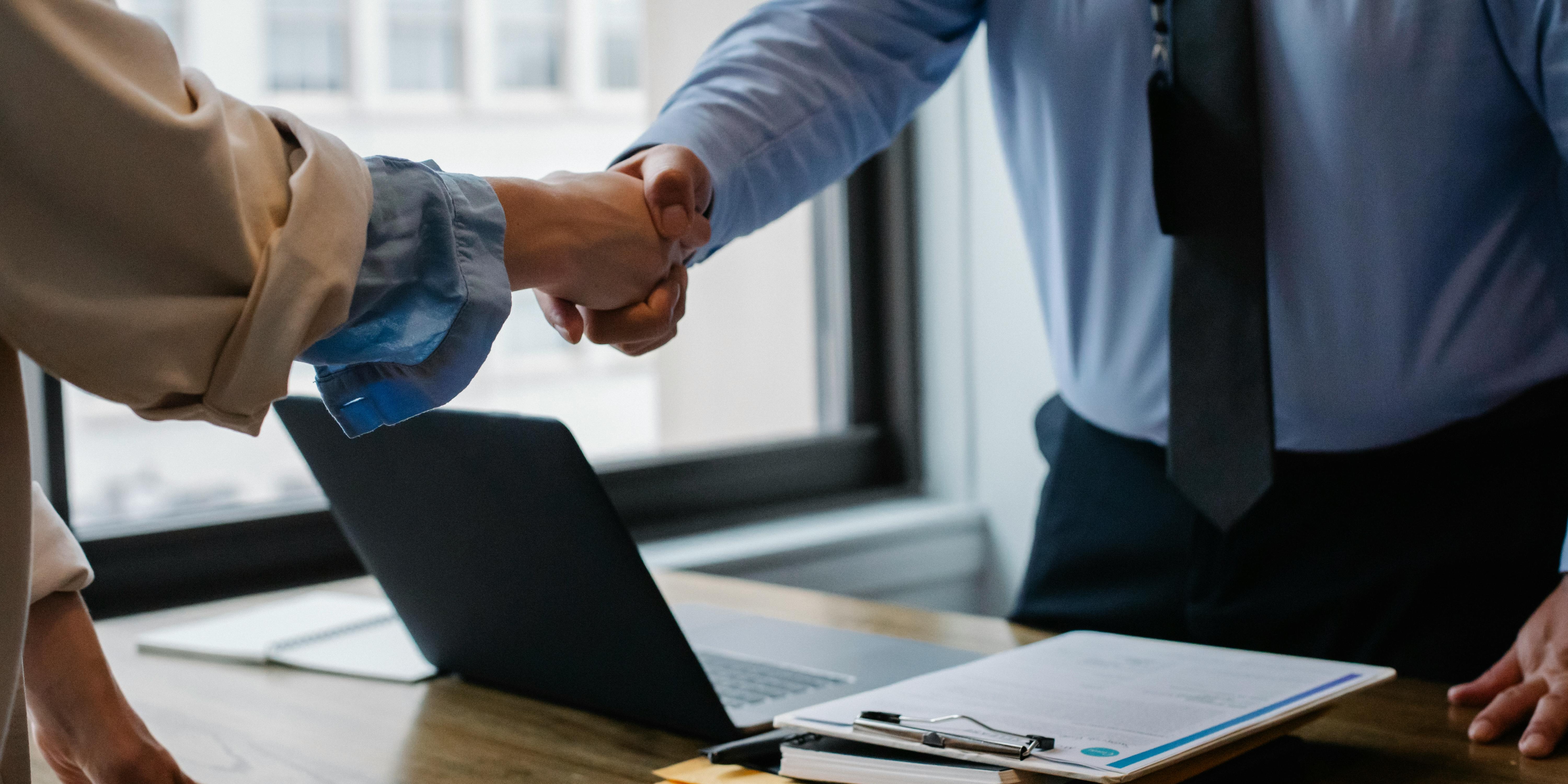 Two people shake hands across a desk