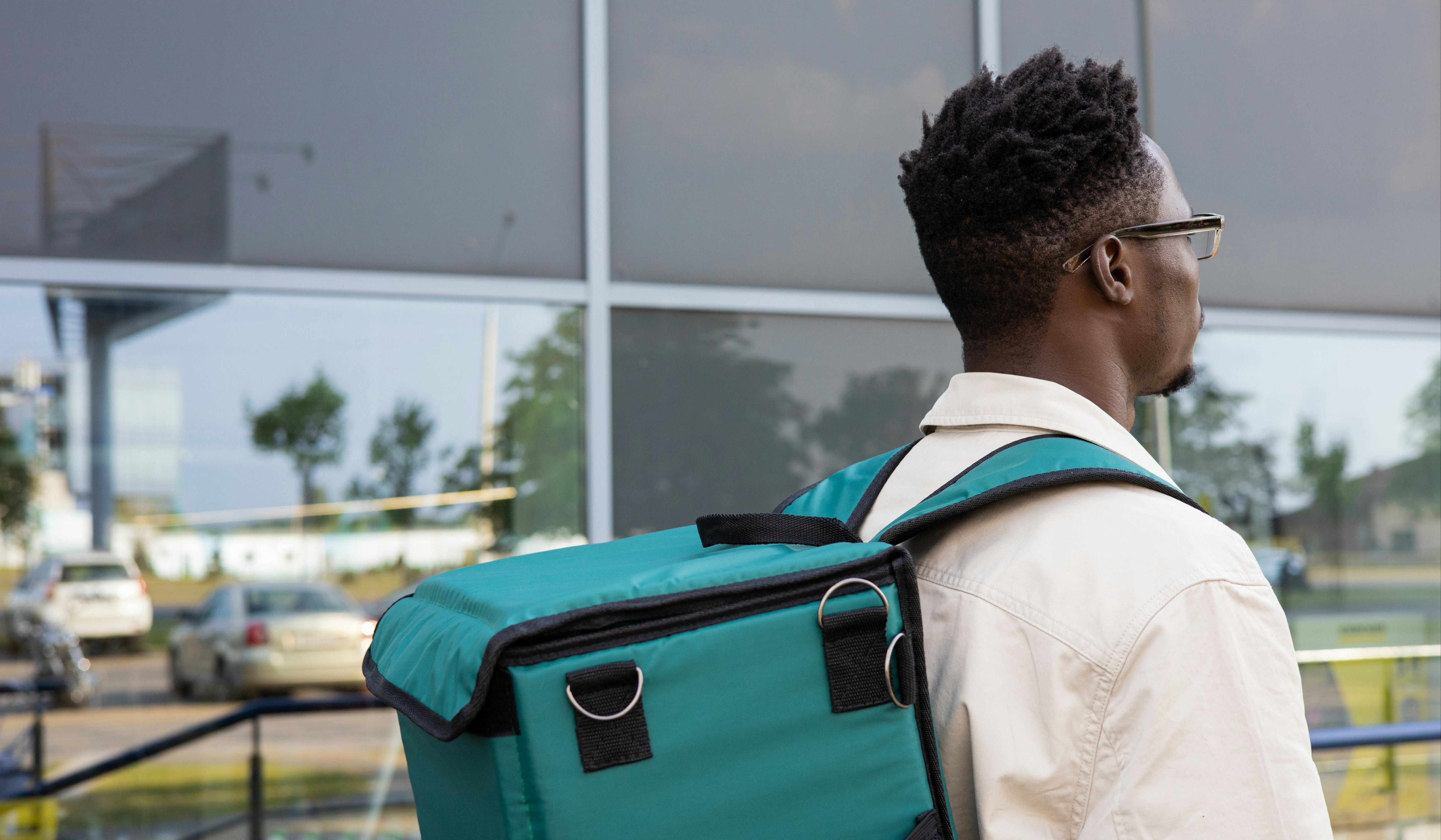 A man walks outside a building with a thermal bag on his back