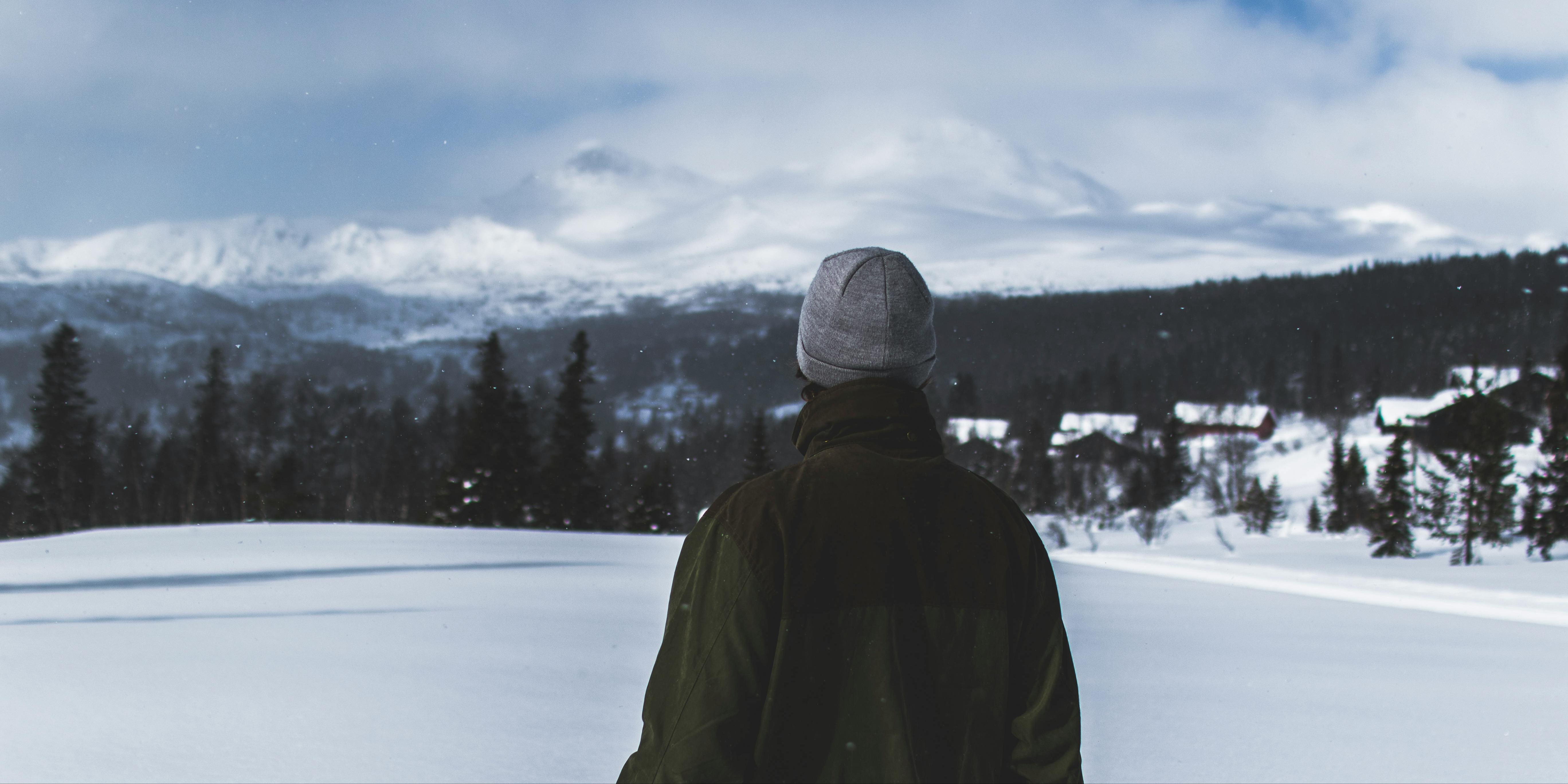 a man, dressed warmly, looks out at a snowy mountain