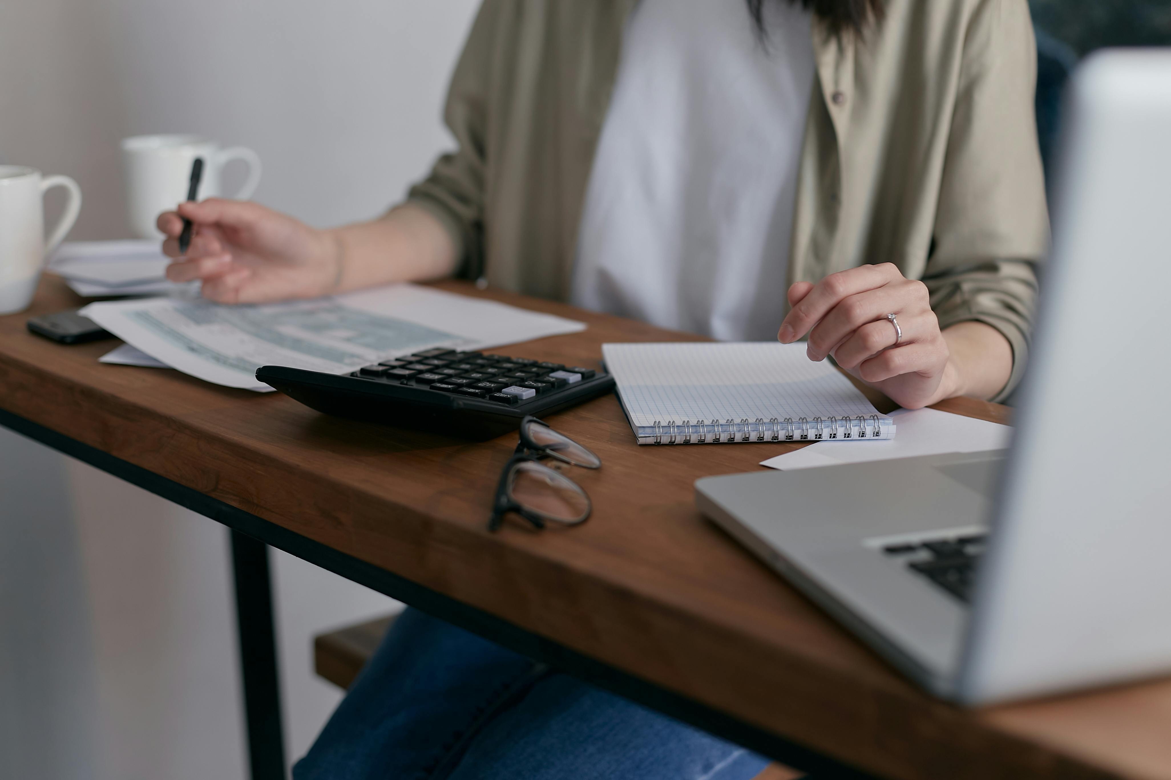 a woman reviews credit statements with a calculator and laptop