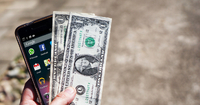 a hand holds a cell phone and a few dollar bills